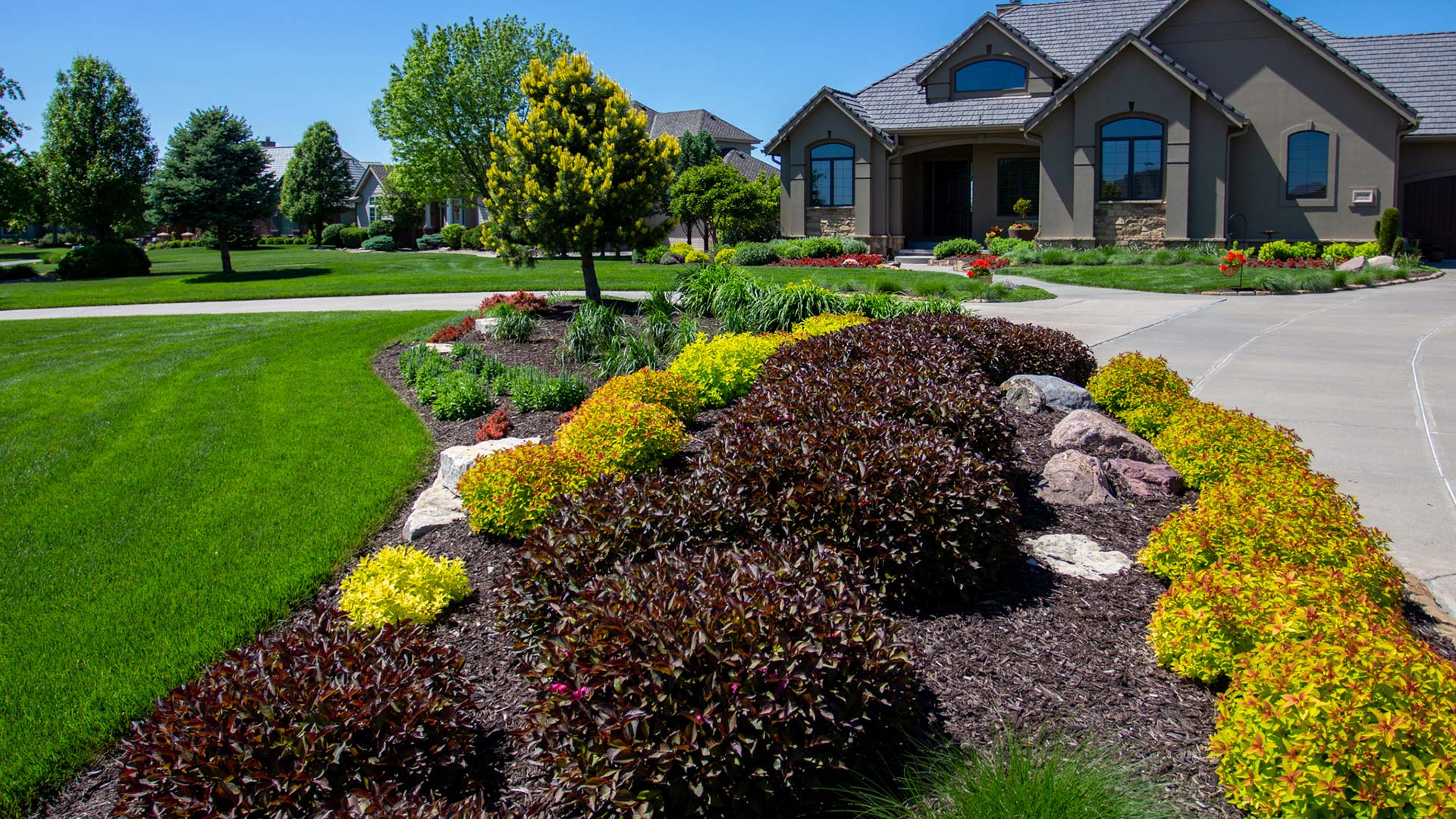 A large landscape bed with colorful bushes and trees near a home in Valley, NE.