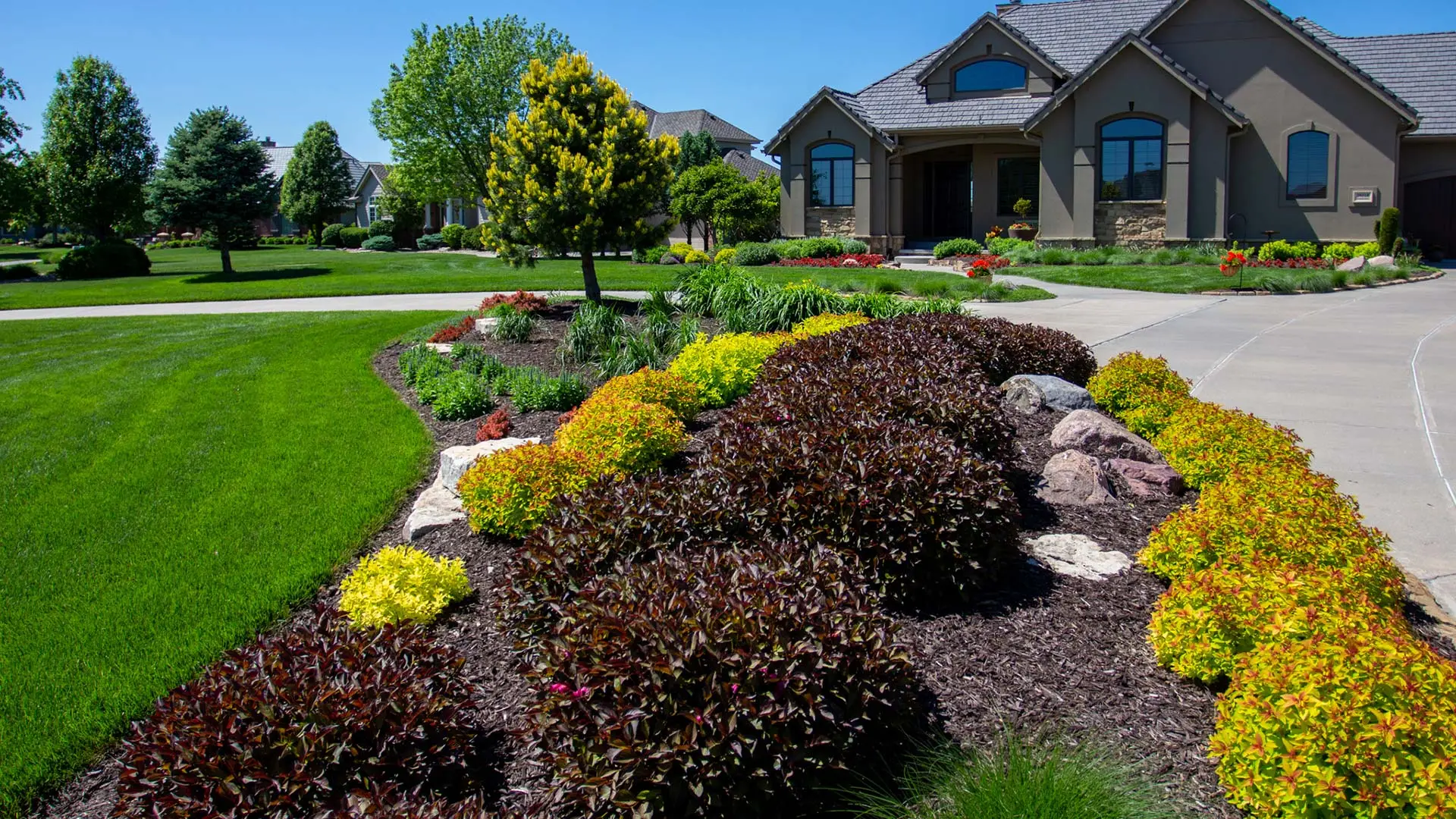 A large landscape bed with colorful bushes and trees near a home in Valley, NE.