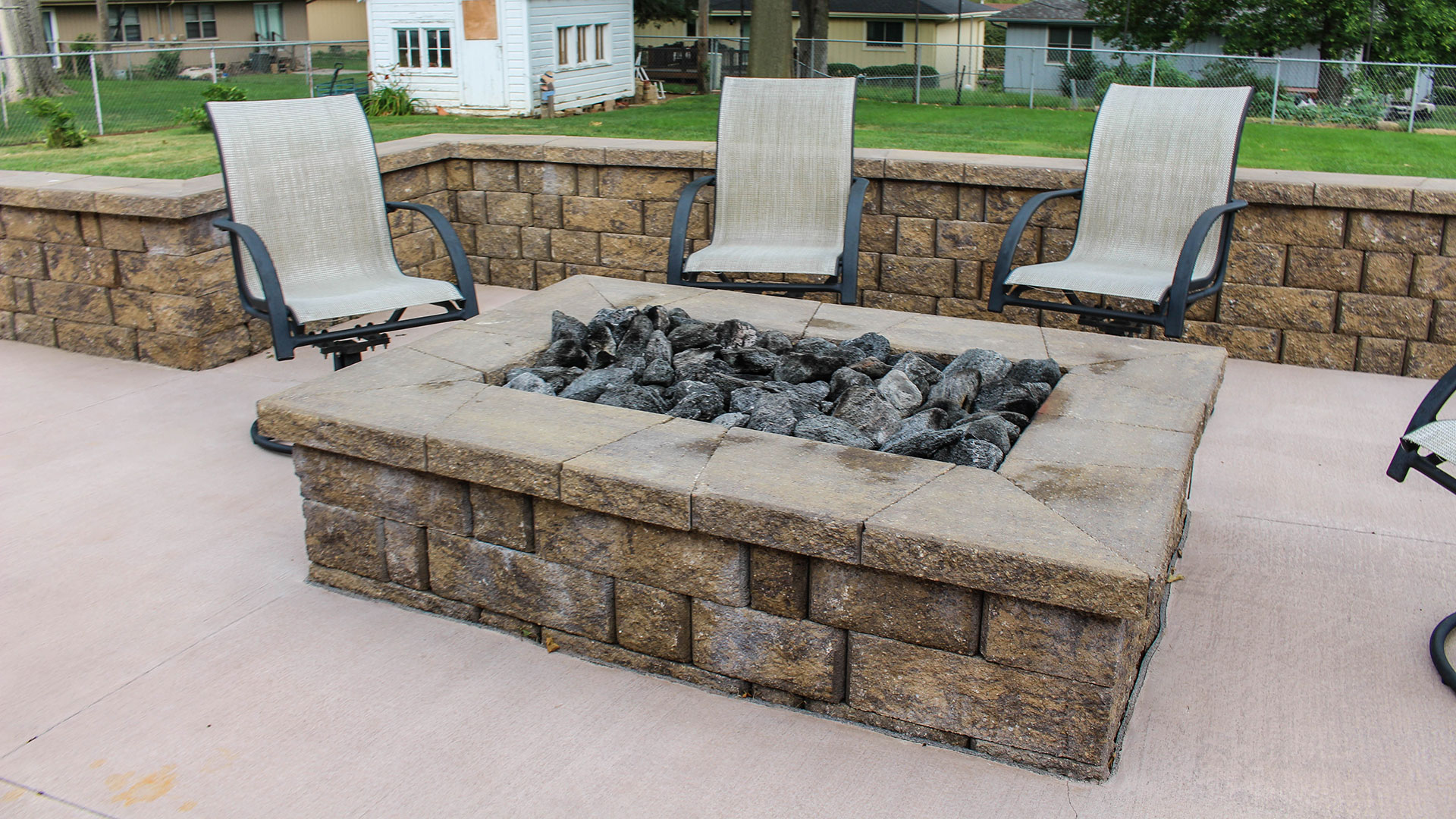 A stone outdoor fire pit on a patio surrounded by chairs and a retaining wall in Gretna, NE.