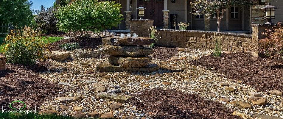 A water feature and plantings surrounded by mulch and rock on a property in Bennington, NE. 
